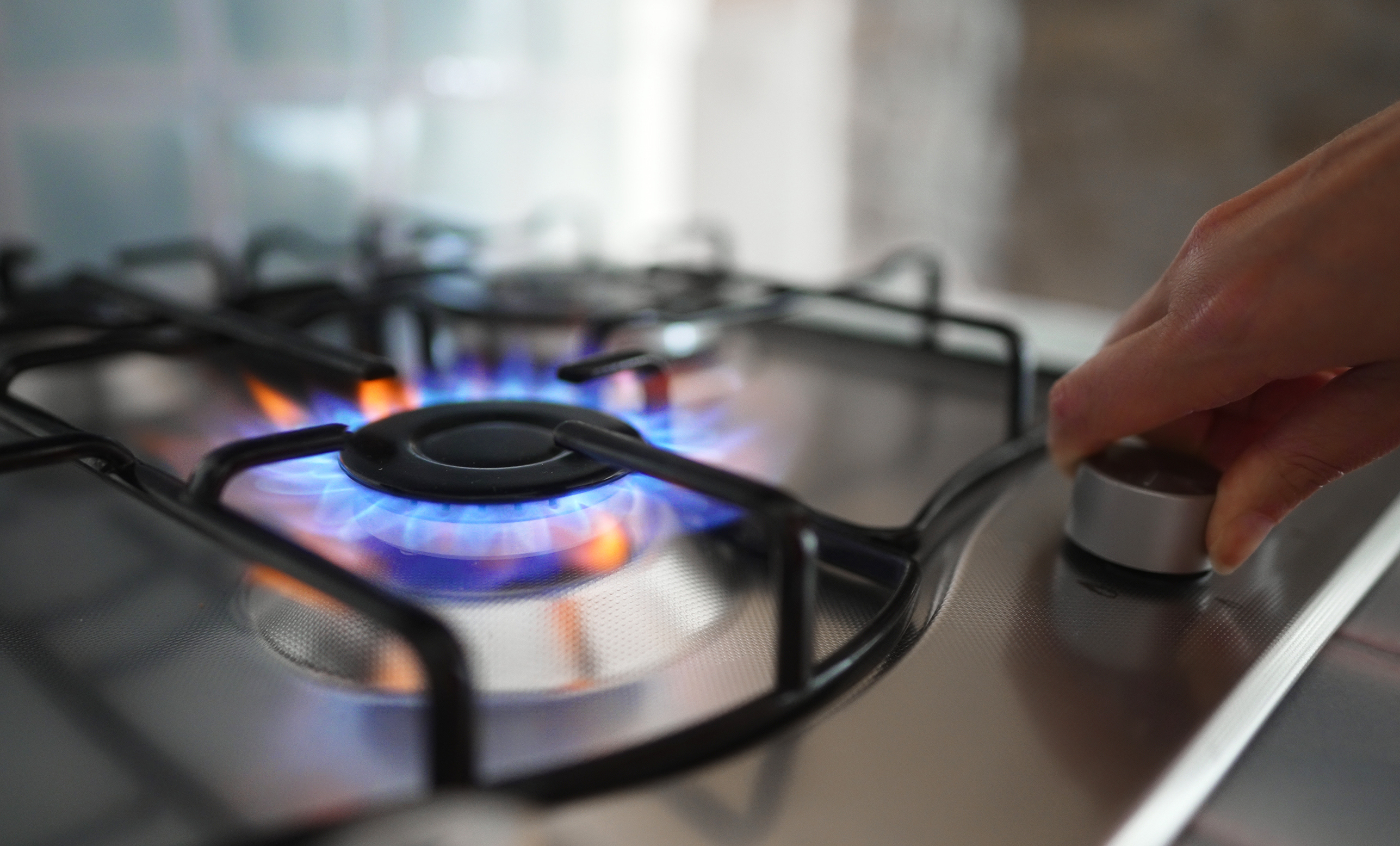 Person adjusting a gas stove burner with a blue flame