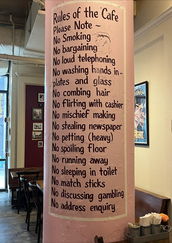 List of quirky cafe rules on a pink pillar including no loud talking, bargaining, or flirting with the cashier