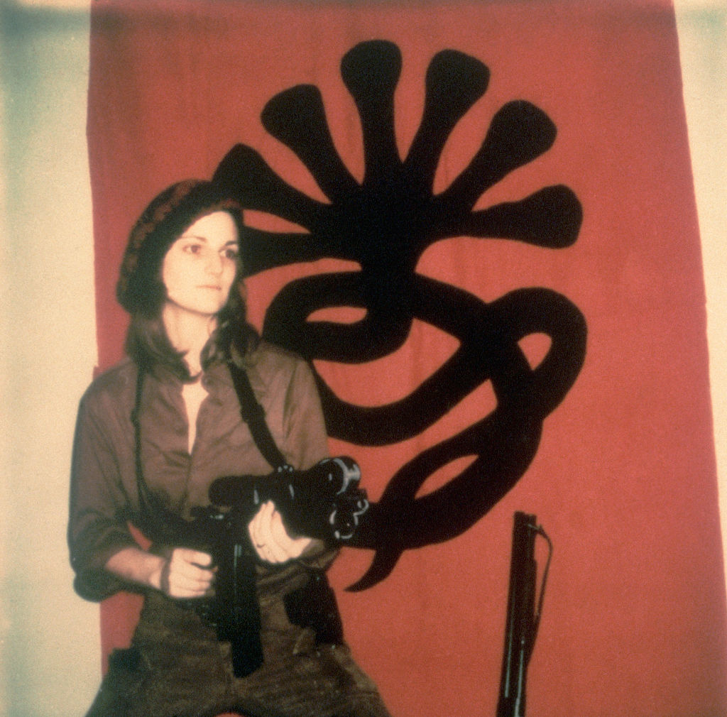 Patty Hearst holding a gun in front of a flag of the SLA