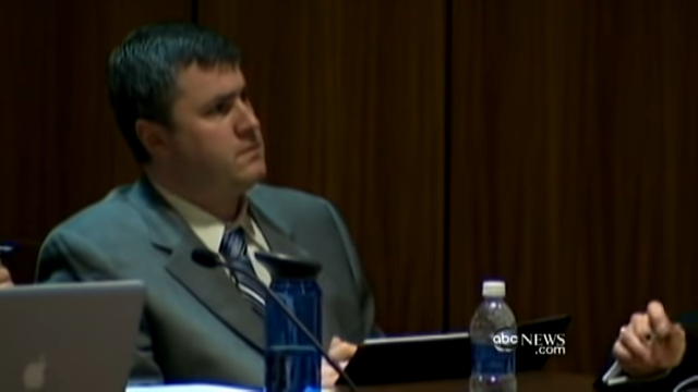Gabe in a suit sits at table with laptop, facing forward in a courtroom setting