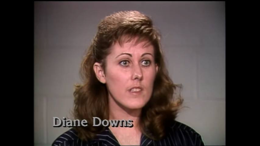 Diane sitting in front of a plain background during an interview; she has curly hair and appears focused