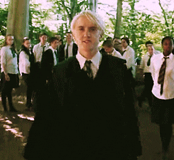 Personaje Draco Malfoy de &quot;Harry Potter&quot; caminando con una expresión desafiante, rodeado de otros estudiantes