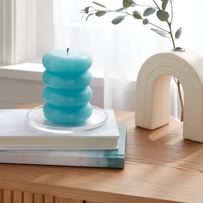 A stackable bubble candle on a book, next to a ceramic arch decor piece on a wooden table