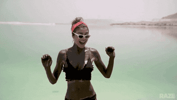 Mujer con top negro y gafas de sol bailando alegremente en la playa