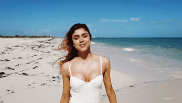 Mujer sonriendo en una playa soleada con un traje de baño blanco