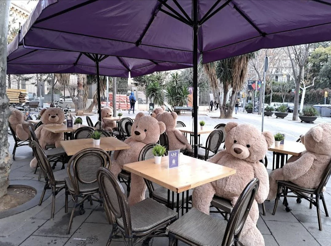 Large teddy bears seated at outdoor cafe tables, simulating a social atmosphere