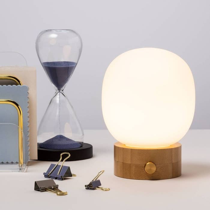 Glowing spherical lamp on a wooden base next to an hourglass and stationary on a desk