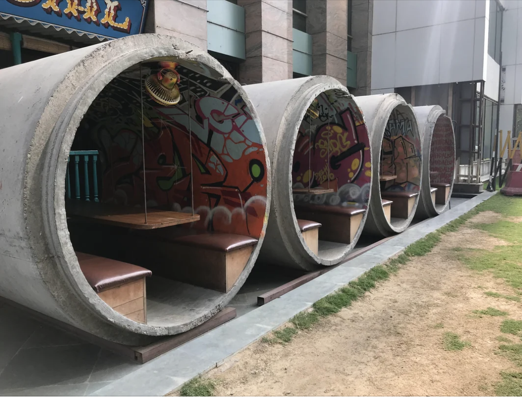 Outdoor dining area with booths set in large concrete pipes, decorated with graffiti art