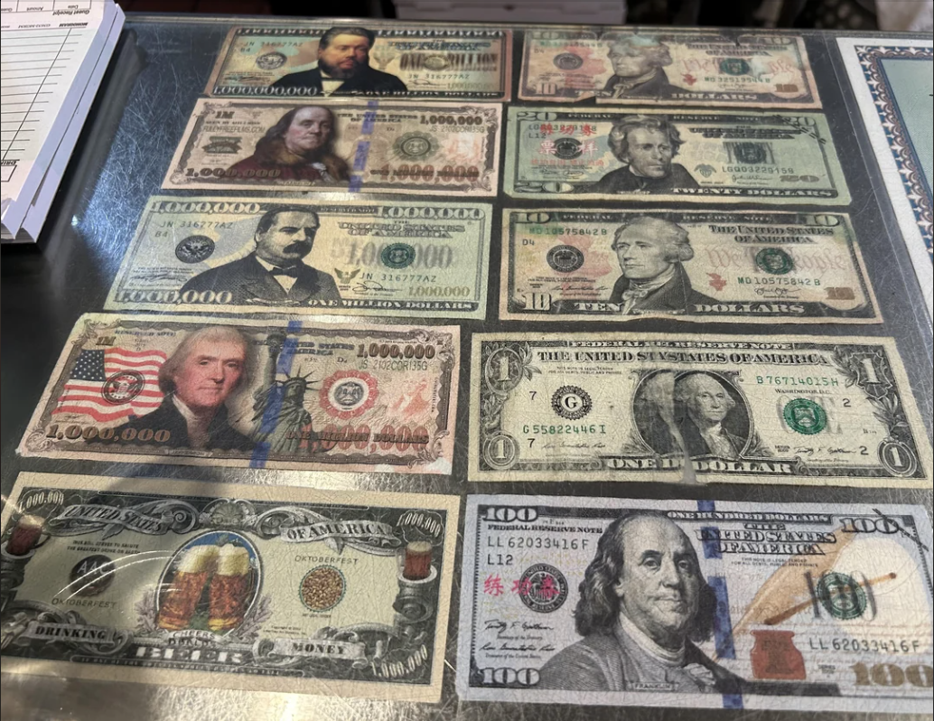 Various novelty US currency bills with high denominations and fictional characters displayed on a table