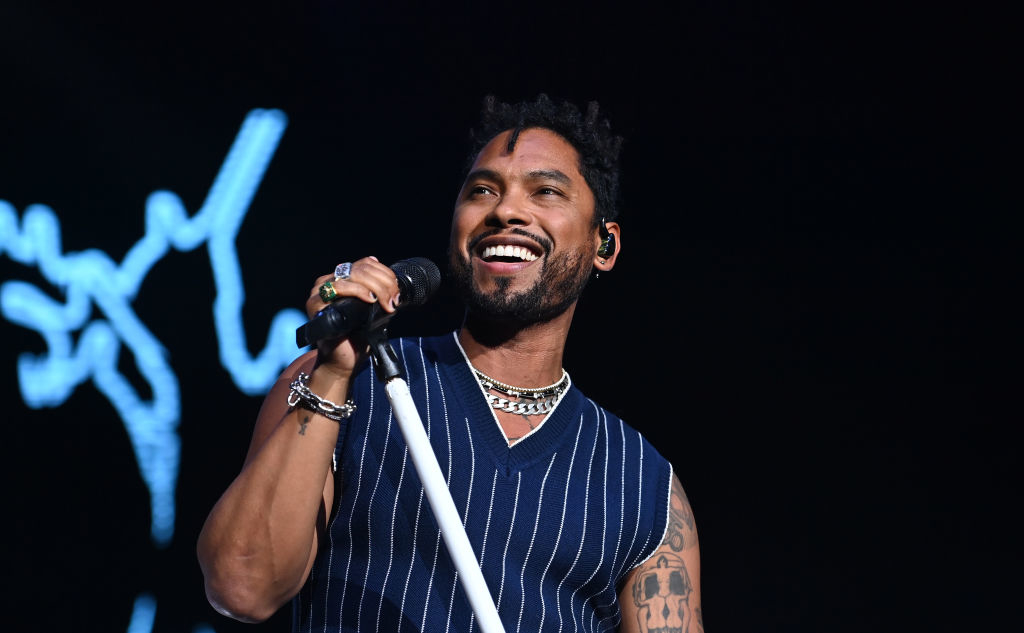 Miguel performs onstage, holding a microphone, with a joyful expression