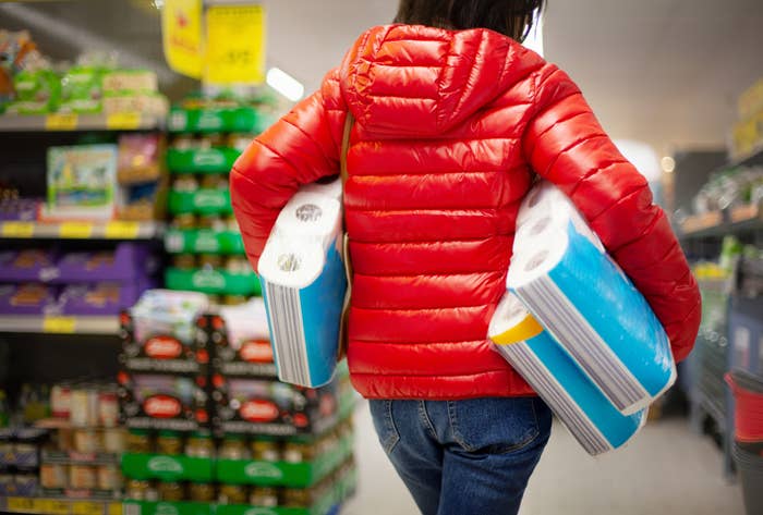 Person shopping, carrying two large paper towel packs under each arm while walking down a store aisle