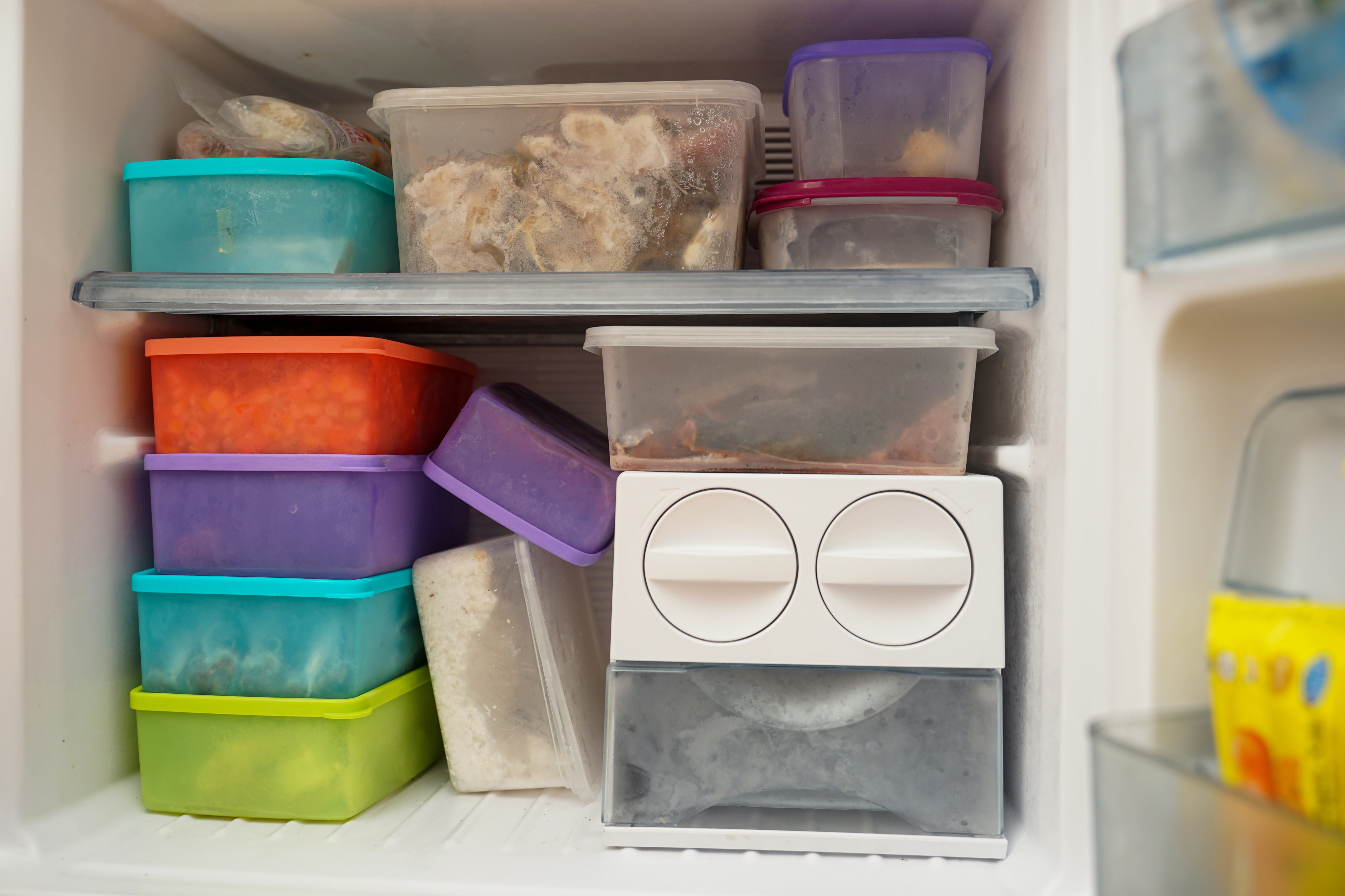 A freezer filled with various stacked food storage containers and an ice cube tray