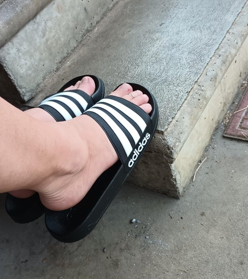 reviewer wearing a black and white striped Adidas slide sandal on a concrete step