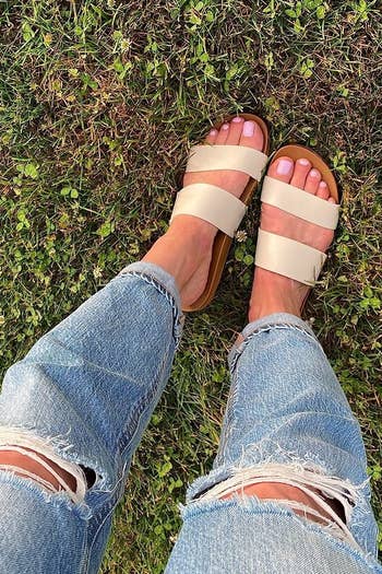 reviewer photo of a person wearing ripped jeans with tan sandals standing on grass