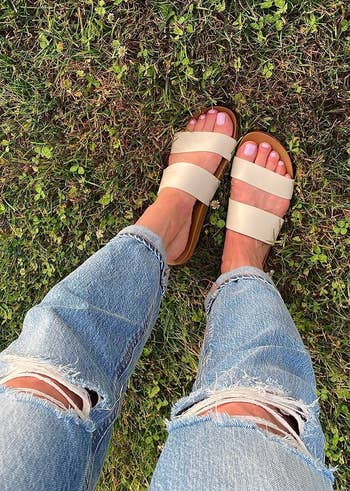reviewer photo of a person wearing ripped jeans with tan sandals standing on grass