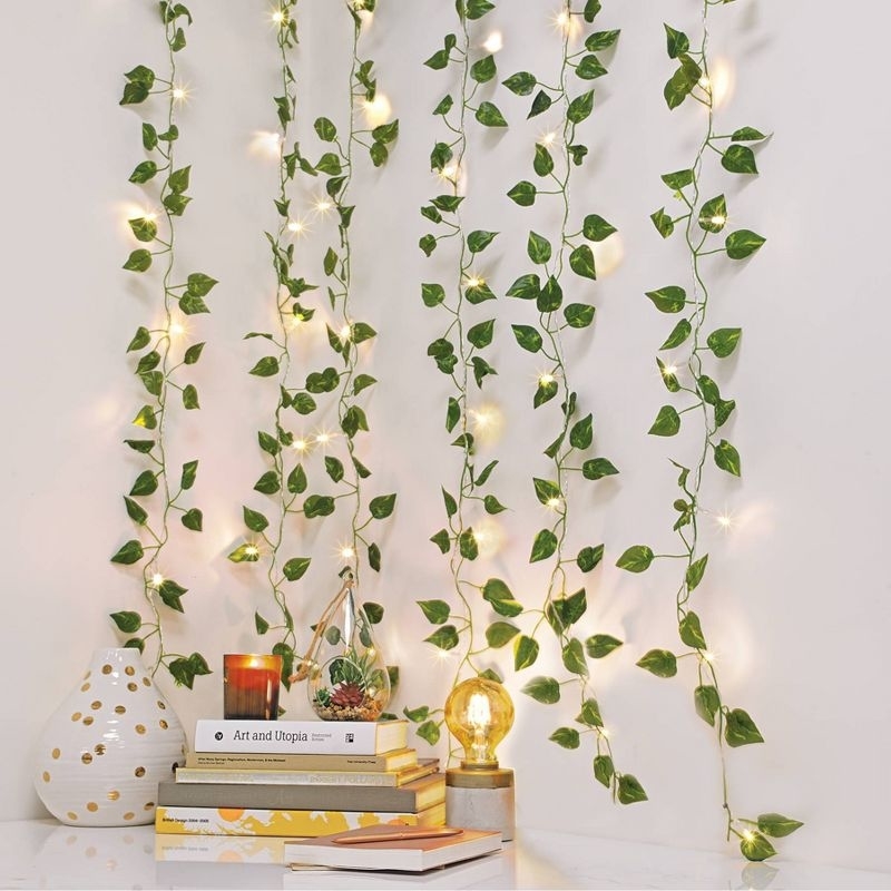 string lights with leaves on a wall above a shelf with books and decorative items