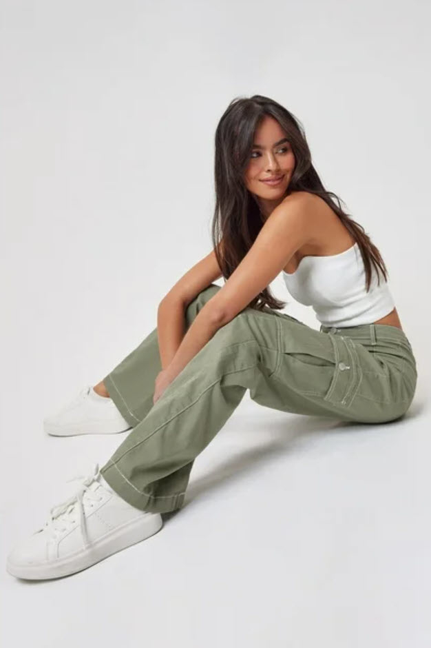 model in white tank top and green cargo pants sitting and looking at the camera