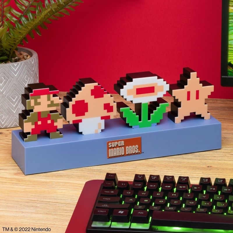 three-dimensional pixel art figures from Super Mario Bros, including Mario, a mushroom, a Piranha Plant, and a star, on a desk