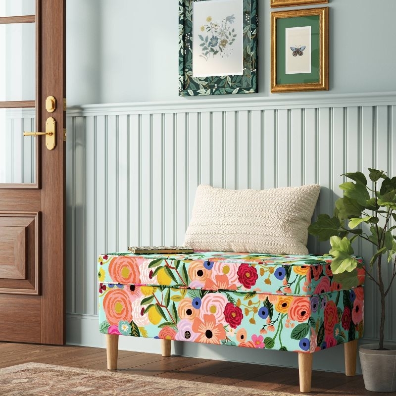 floral storage bench with cushion in a room with framed artwork on the wall and a wooden door
