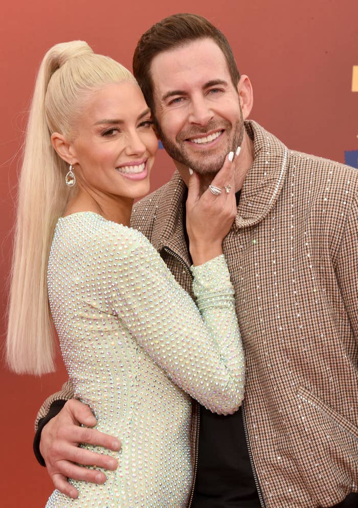 Two people, one with long blonde hair in a bejeweled dress and the other with a beard and checkered jacket, smiling and posing closely