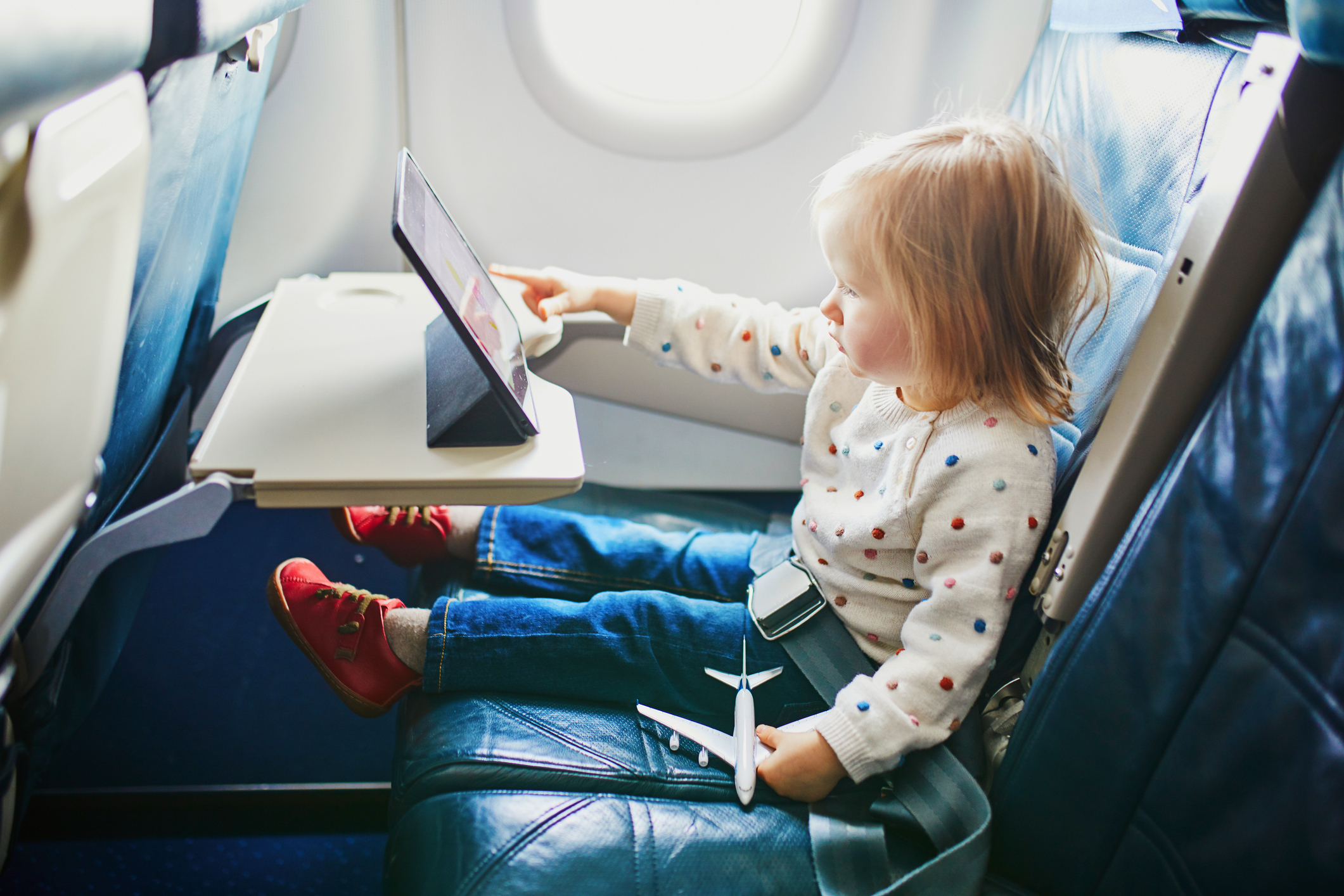 Toddler in a seat playing with a tablet and a toy airplane