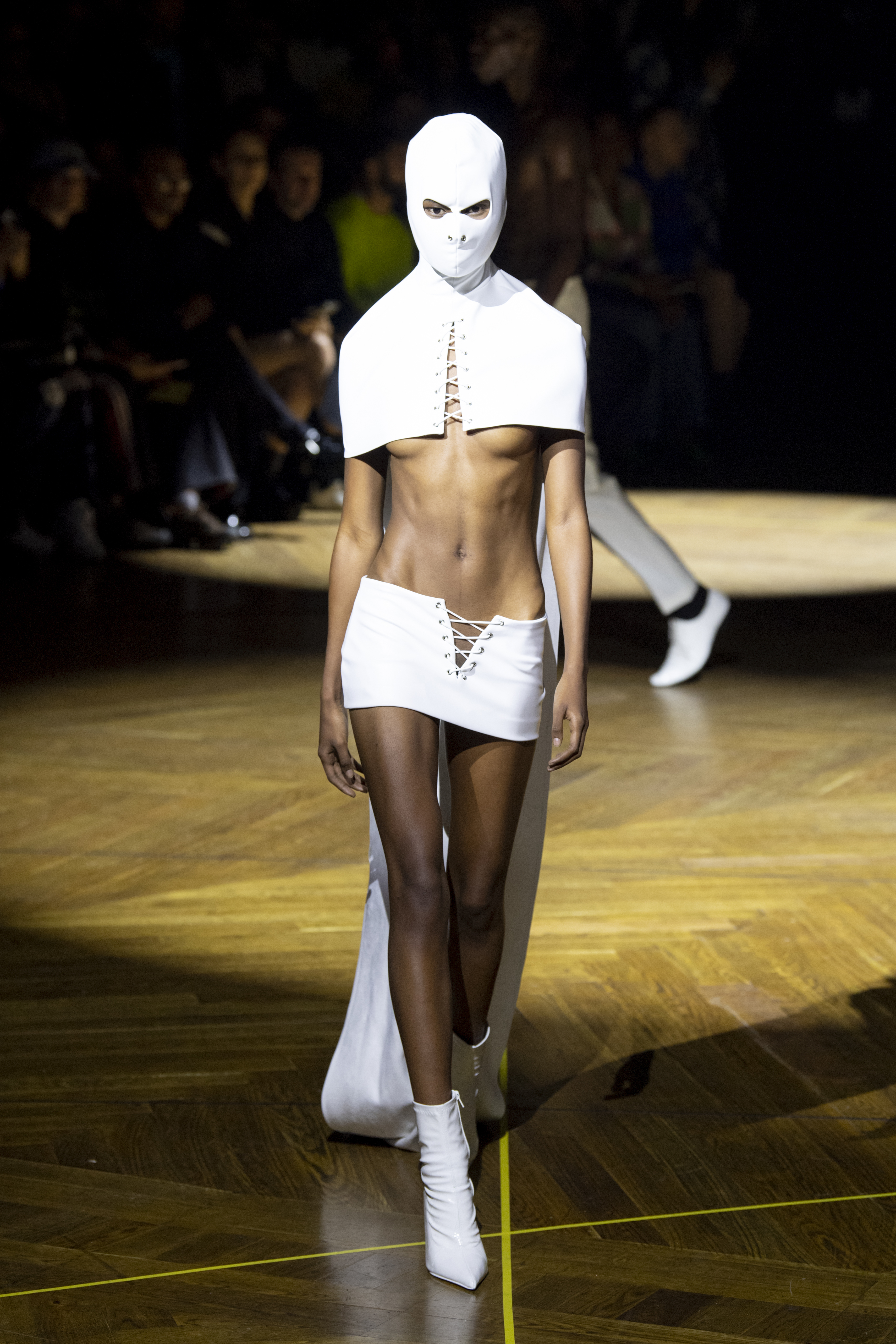 Model on runway in white avant-garde outfit with face fully covered by mask