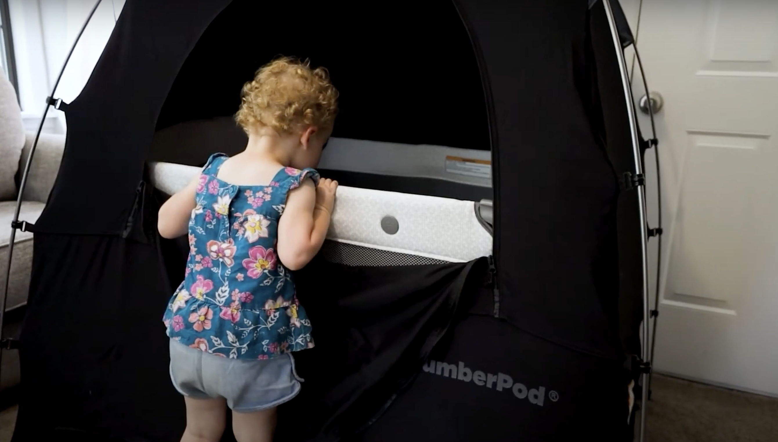 Toddler standing by a portable SlumberPod tent with a crib inside