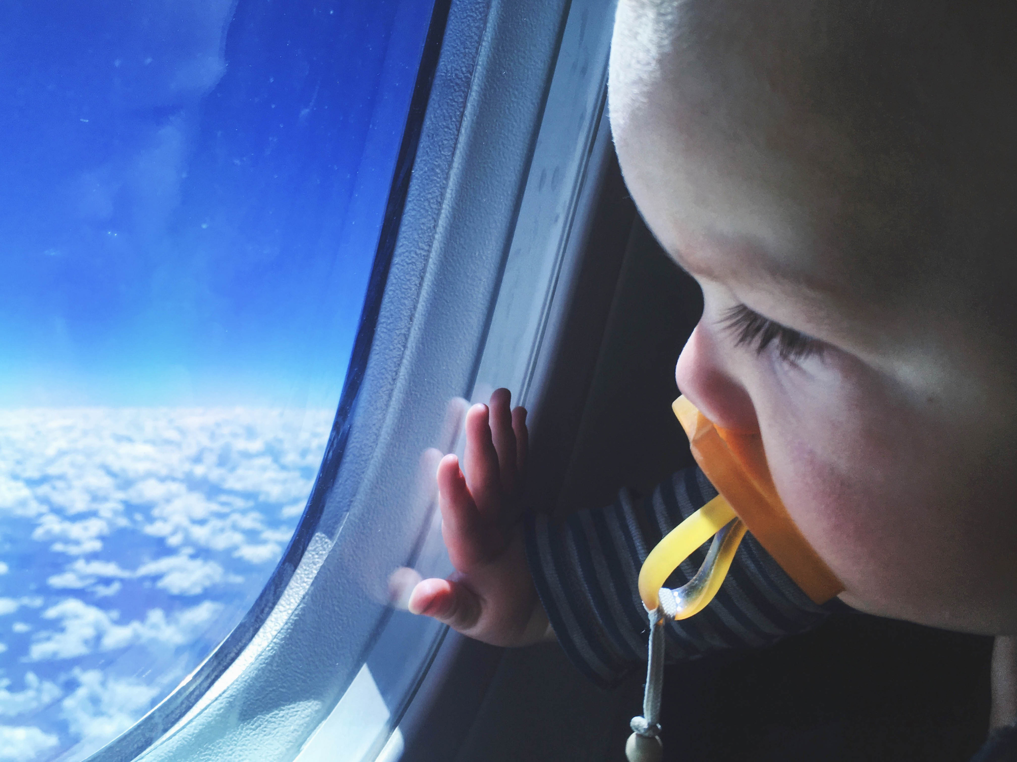 Toddler with a pacifier looking out an airplane window