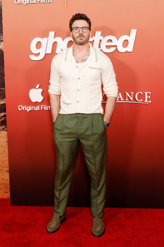 Chris in glasses poses in a cream cardigan, green pants, and matching shoes at a film event