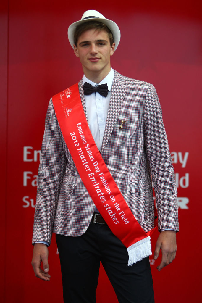 Person wearing a patterned suit, bow tie, and fedora, with a &quot;2019 Epsom Derby - Stewards&#x27; Emirates Melbourne Cup&quot; sash