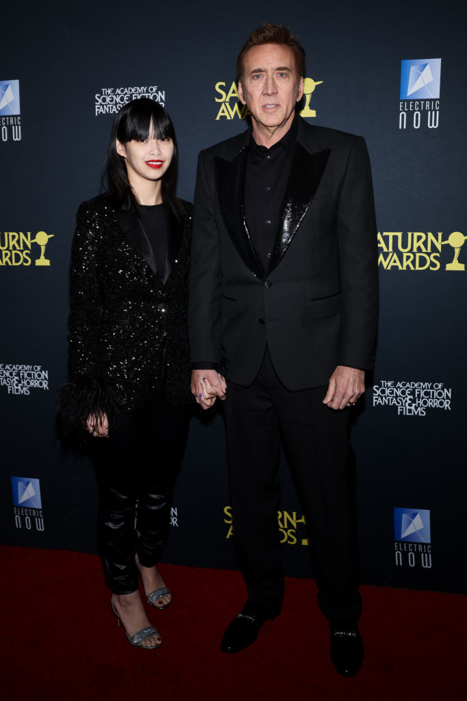 Nicolas and his wife holding hands on the red carpet; she&#x27;s in a sequined pantsuit, he&#x27;s in a suit with satin lapels