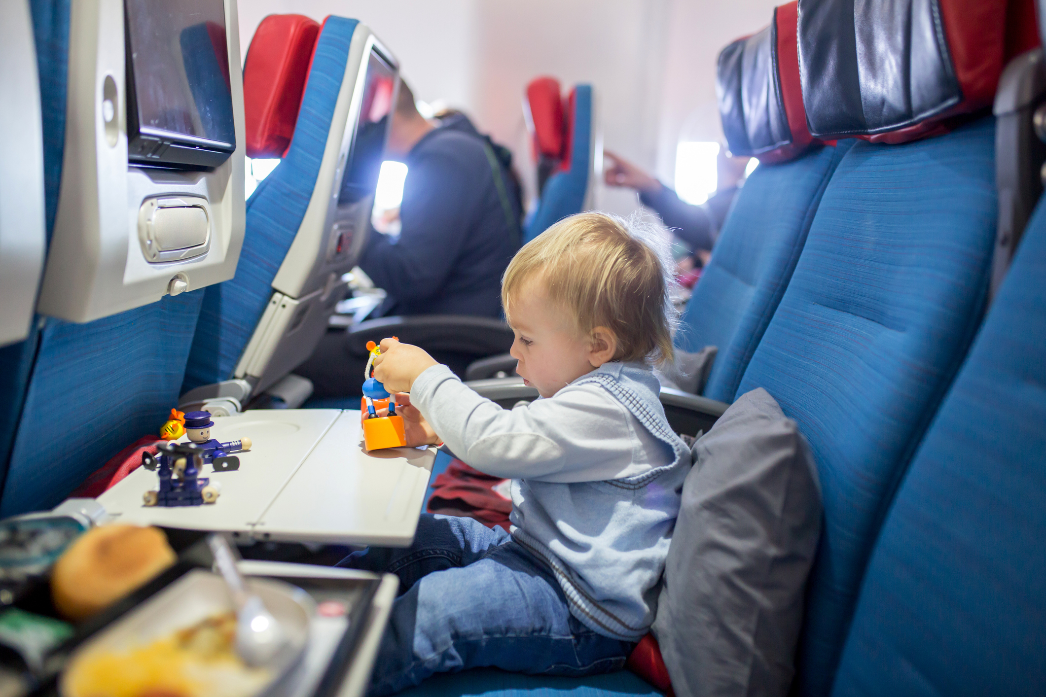 Child playing with toys on airplane tray table, seated in cabin