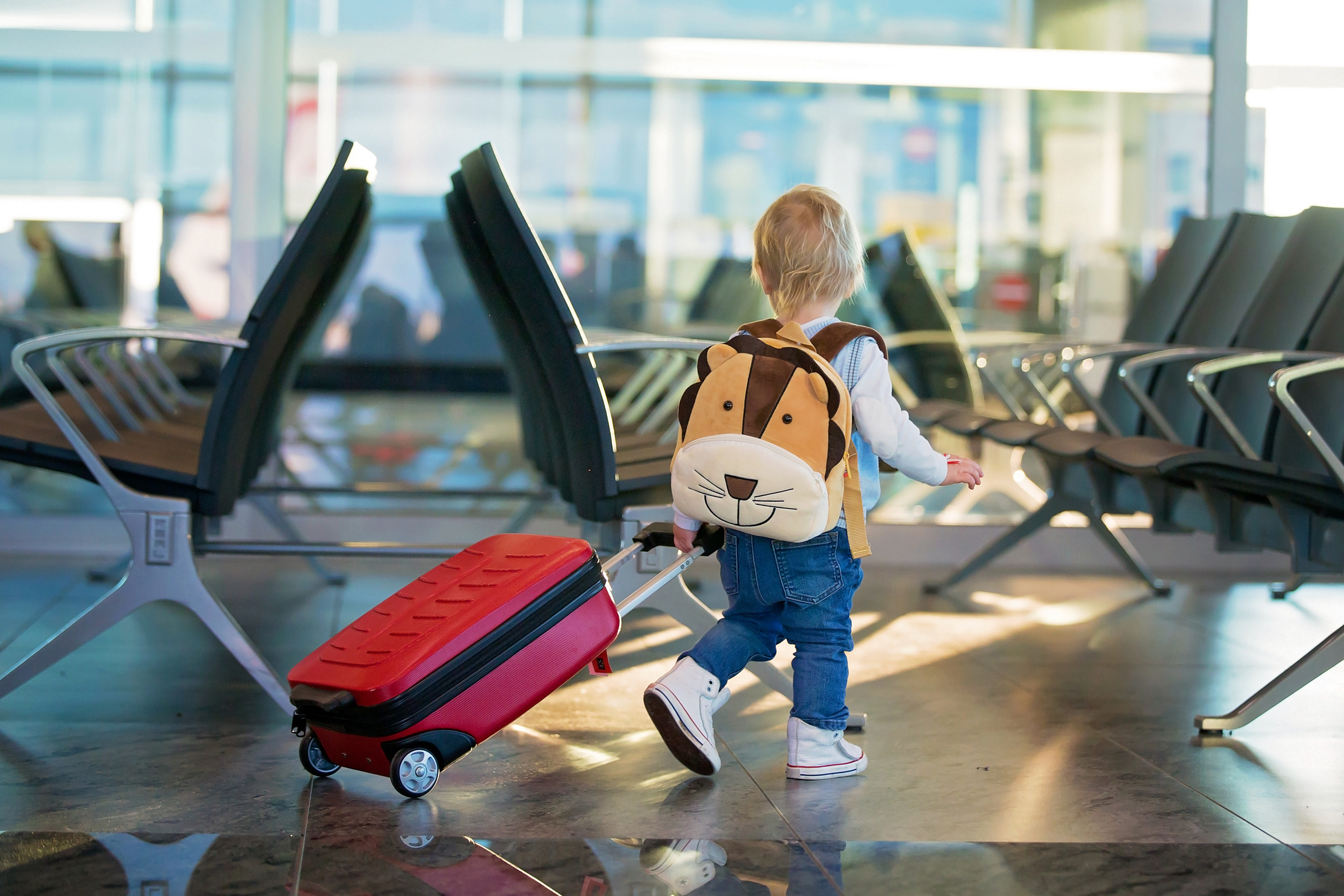 Child with animal backpack pulling a suitcase in an airport waiting area