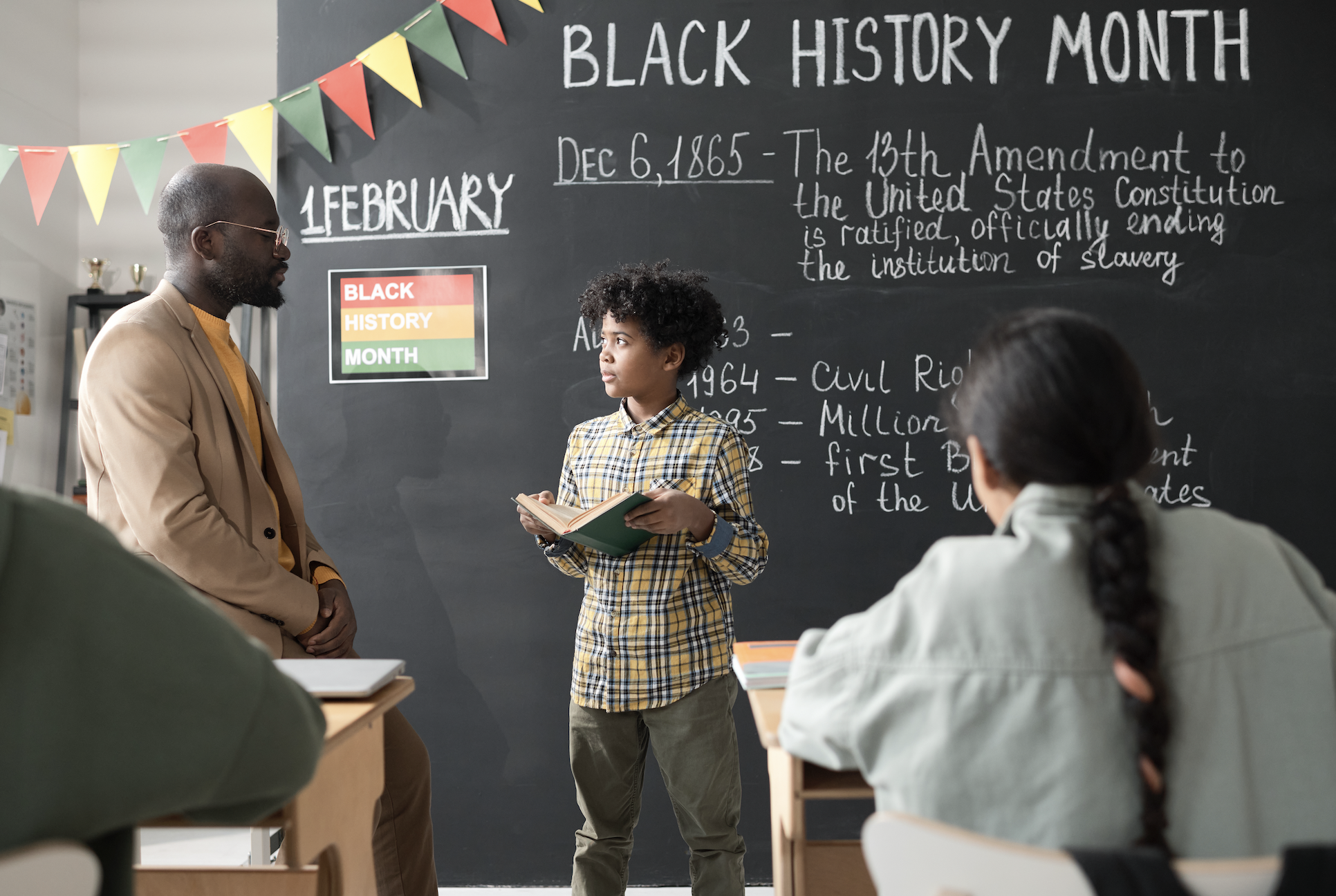 Child presents a book report to adults in a classroom decorated for Black History Month