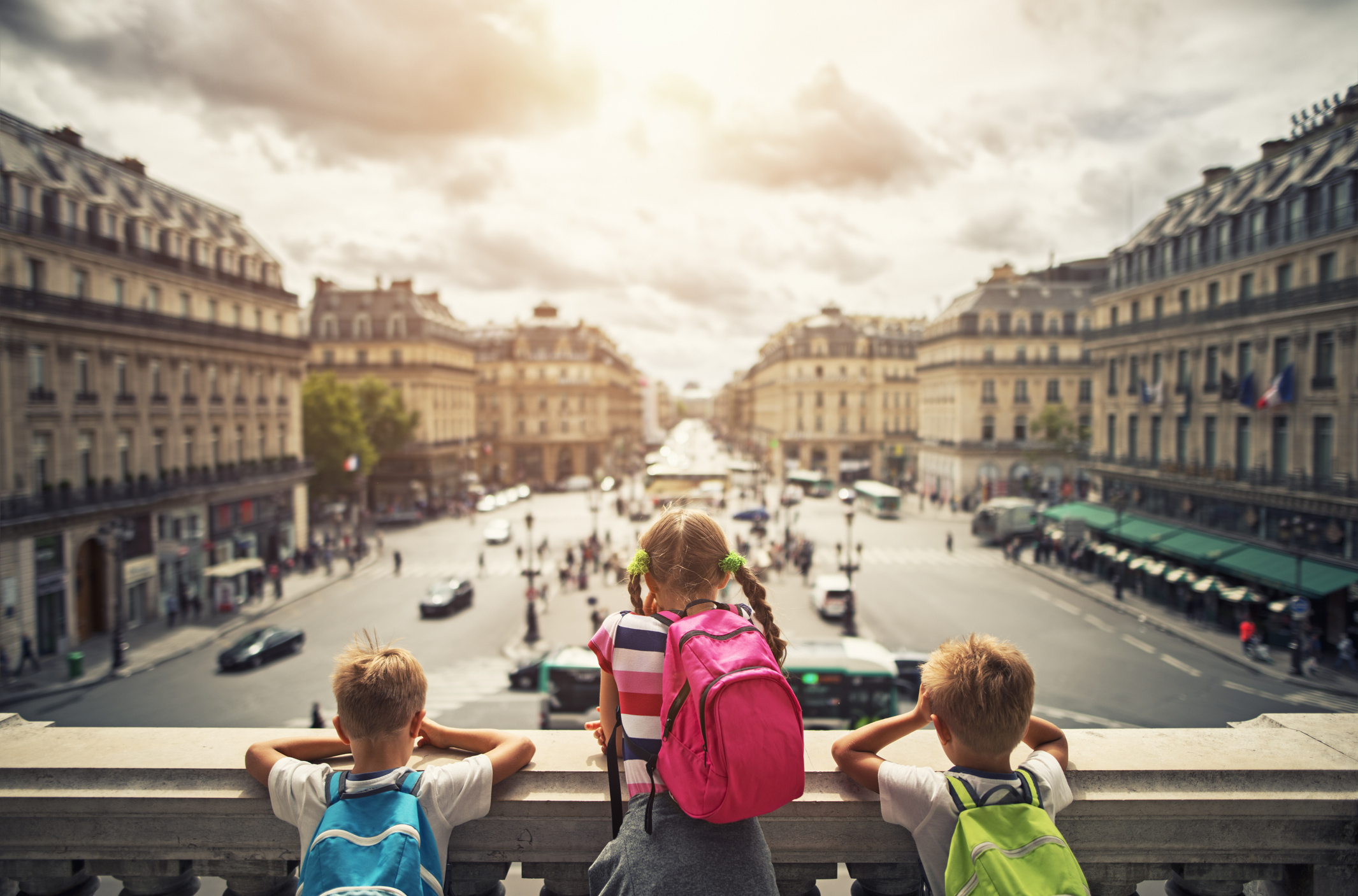 Three children with backpacks looking out over a busy city street from a high vantage point