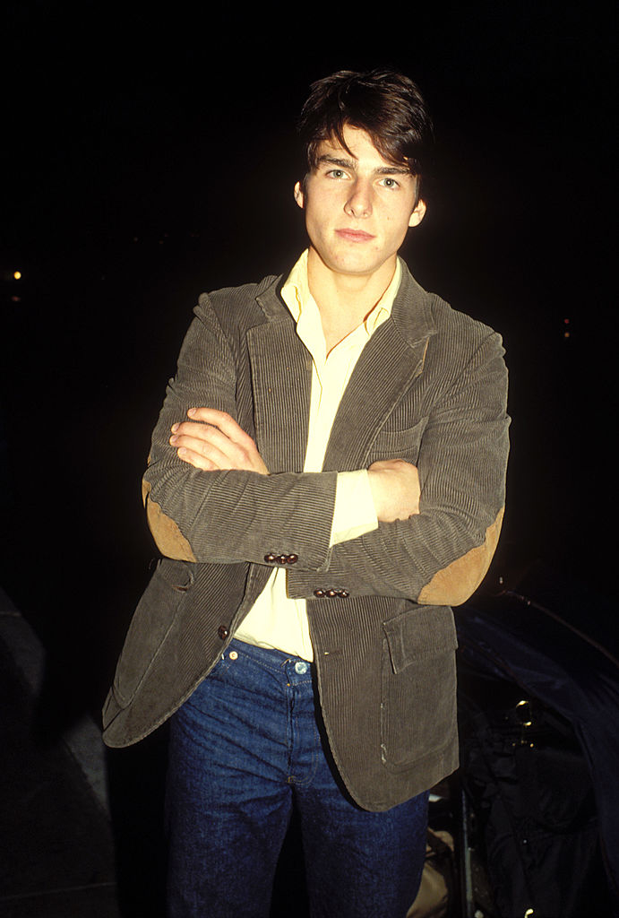 Tom in a striped blazer and jeans, standing with crossed arms