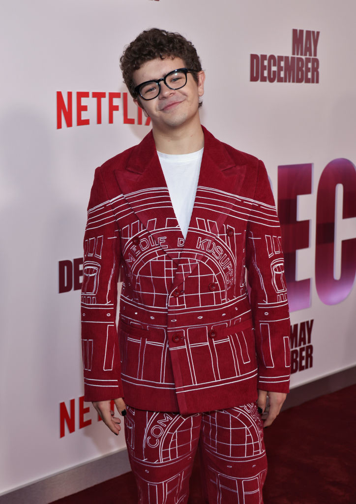 Gaten poses on the red carpet in a patterned red and white suit