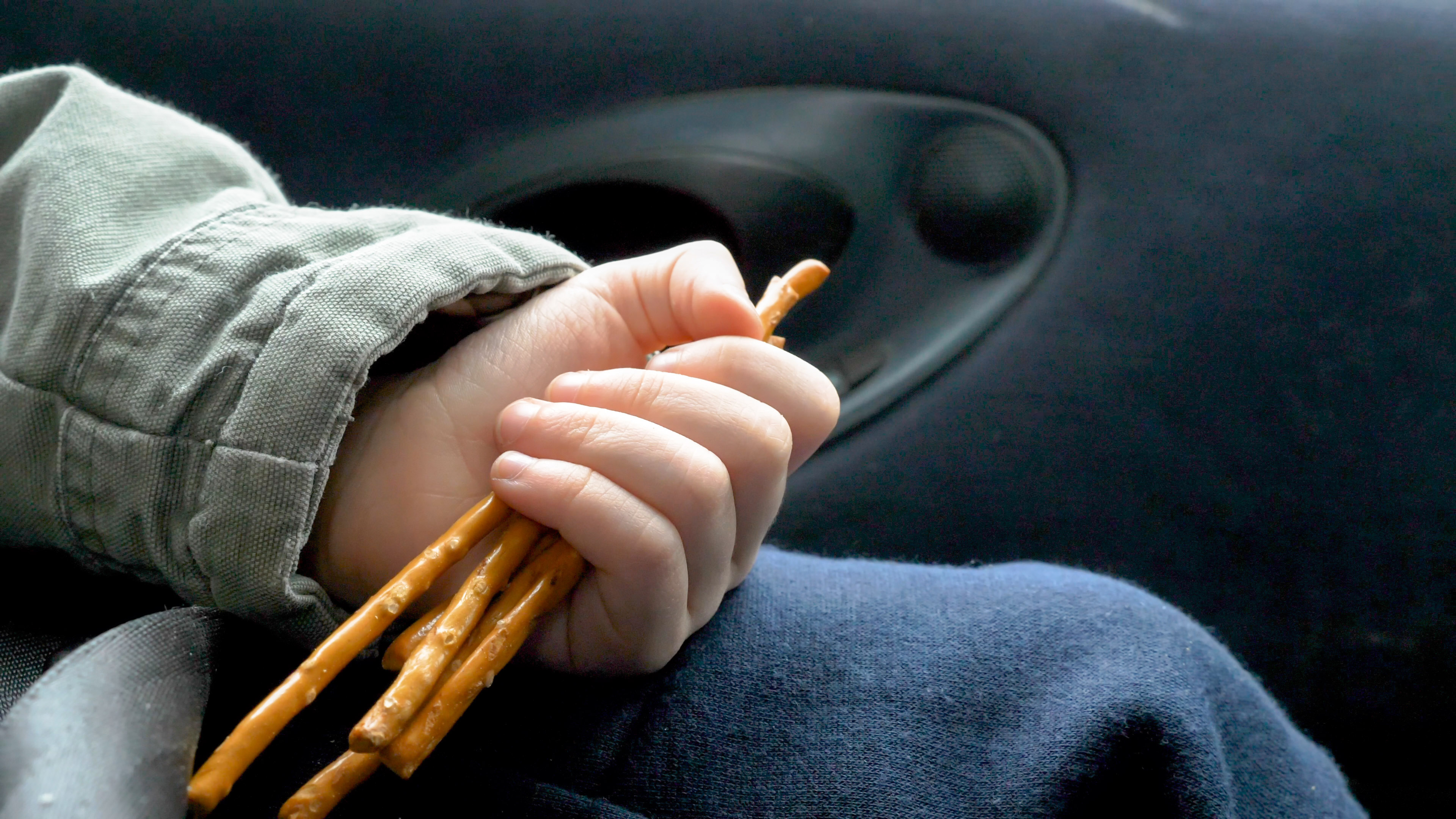 Child&#x27;s hand clutching pretzel sticks while sitting in a car seat