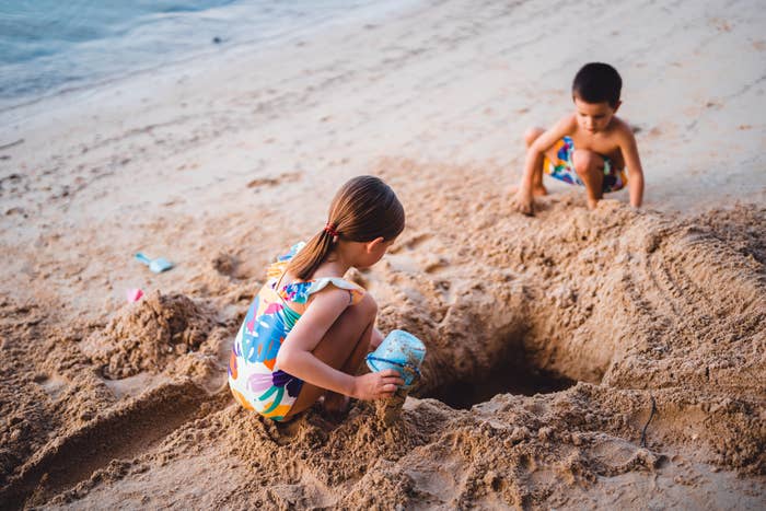 Two children playing in the sand on a beach, digging with plastic shovels