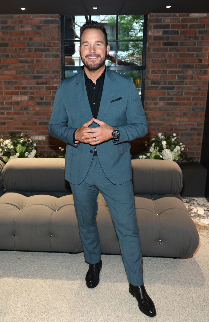 Chris in a tailored suit posing with hands together, smiling at a formal event