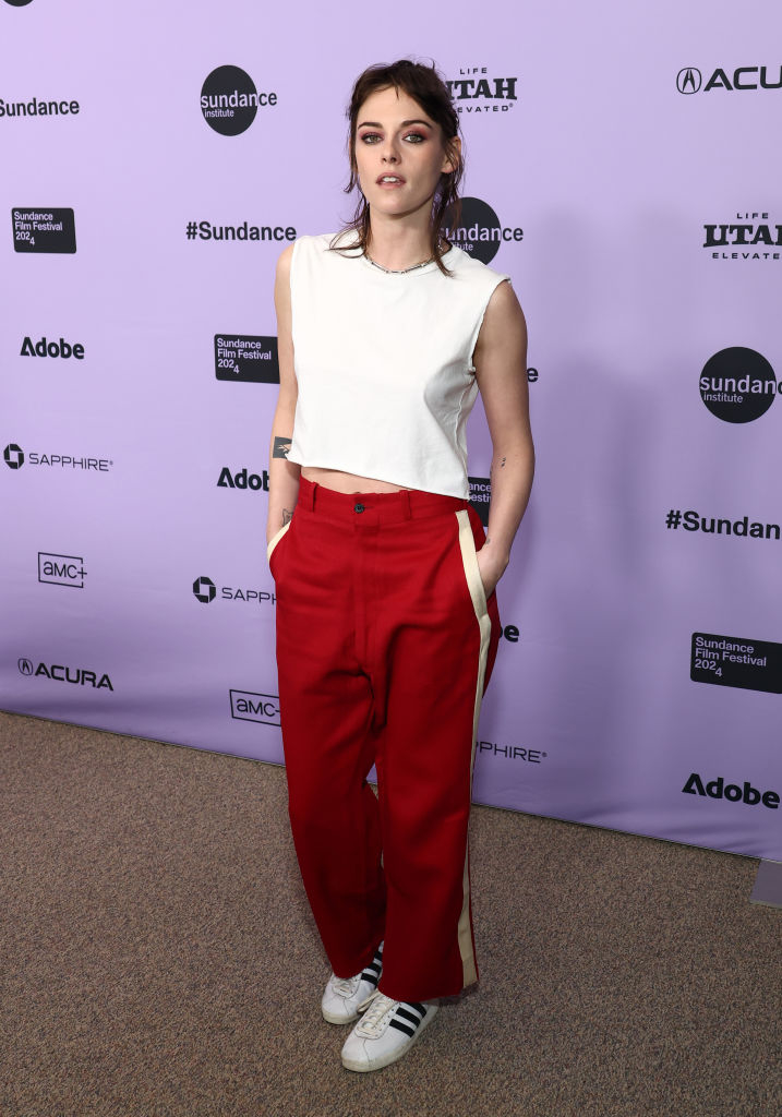 Kristen in a white sleeveless top and red trousers poses at Sundance event