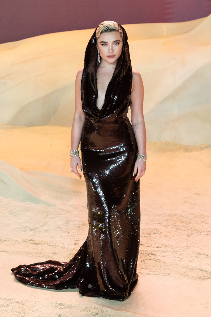 Florence in a shiny, sleeveless floor-length gown with a deep neckline, accessorized with a headpiece and bracelet