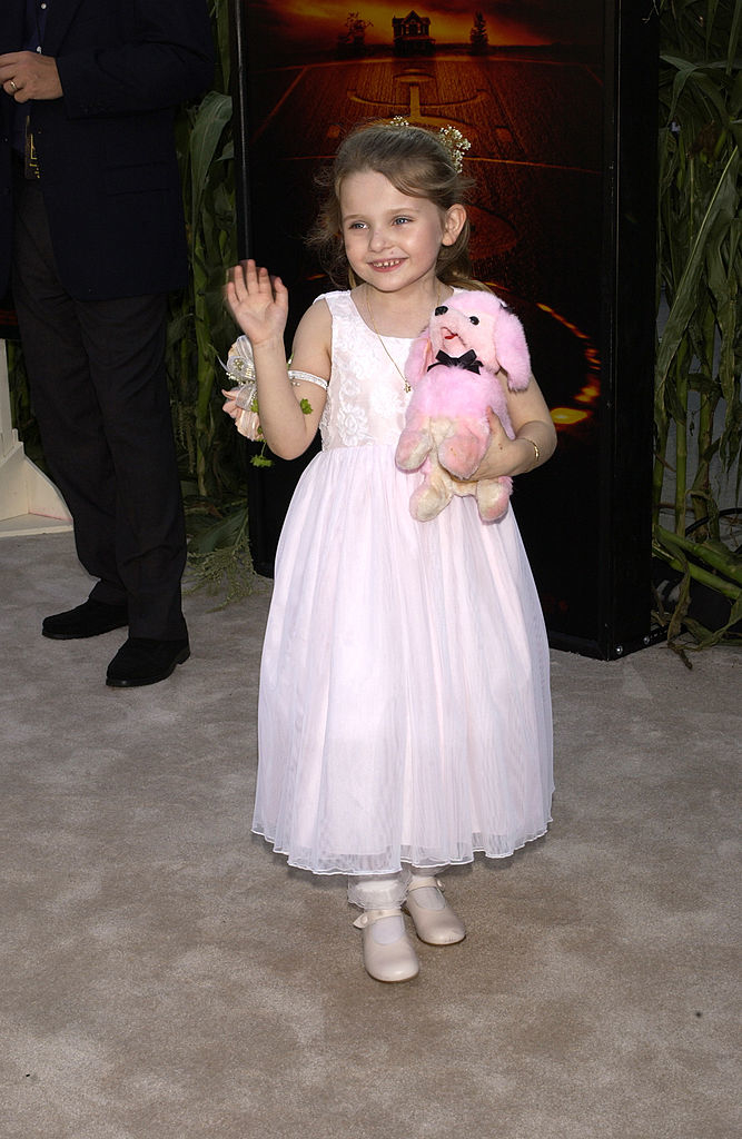 Abigail as a girl in a flowing dress poses with a plush toy on the red carpet