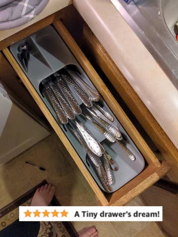 An open kitchen drawer with a silverware organizer containing knives, forks, and spoons