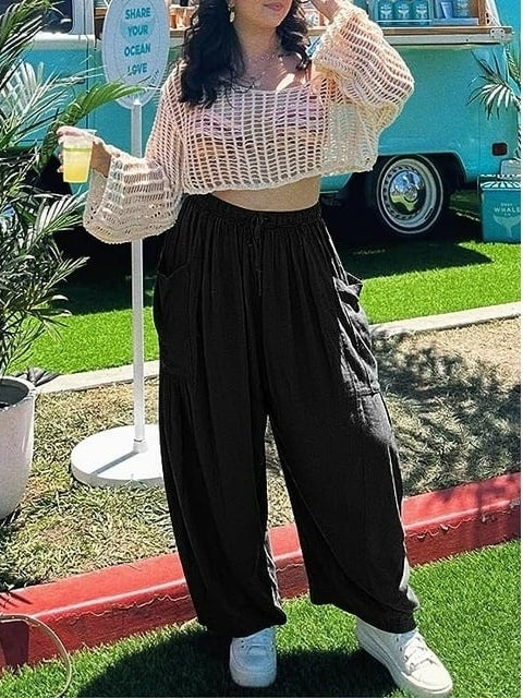 Person in a crochet top and wide-leg pants standing by a vintage camper