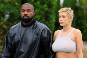 Kanye West in a black jacket and pants beside a woman in a gray sports crop top and leggings, both walking