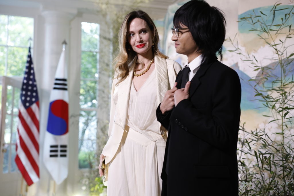 Angie in a white outfit with one of her children standing next to flags