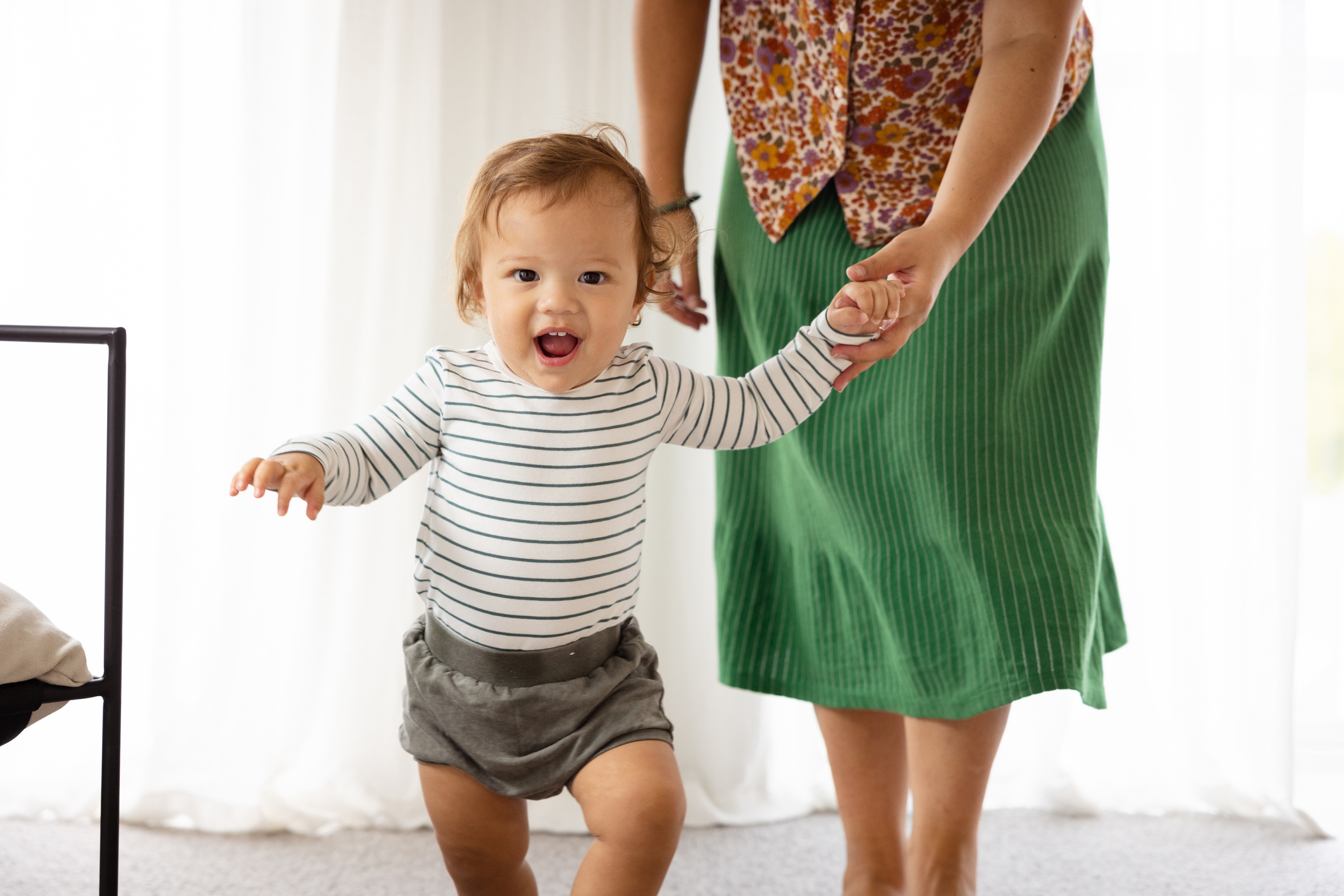 Toddler taking steps holding an adult&#x27;s hand, expressing joy and achievement