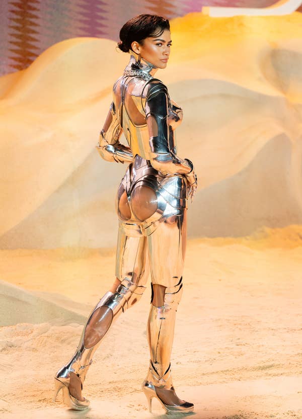 Zendaya in a futuristic metallic outfit posing against a sandy backdrop