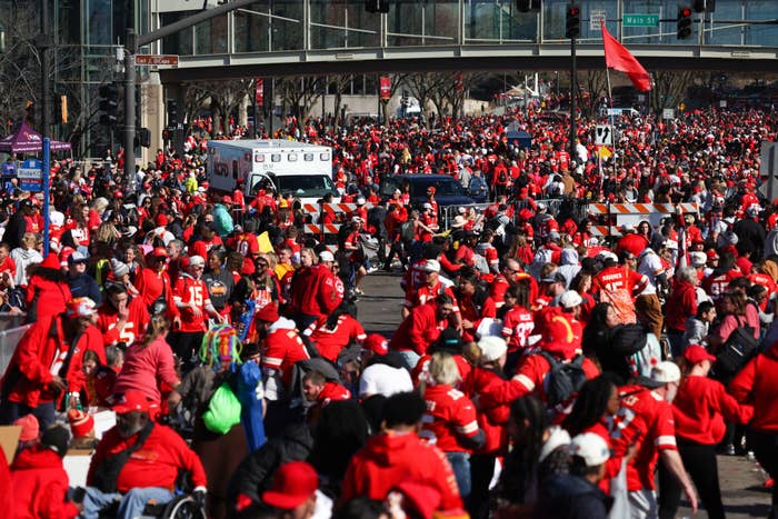 Crowd of fans in team gear celebrating at a sports victory parade. An ambulance tries to make its way through the crowd.